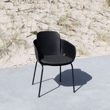 Svart ute stol med anpassad sittdyna från sackit på en solbelyst uteplats vid sanddyner med strandgräs