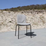 Grå uteplatsstol från sackit på en solig betongyta framför sanddyner med ergonomisk sits och svart metallunderrede för nordiskt utomhusliv