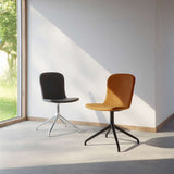 Två sackit Chair no One S1 matstolar med svängbara metallunderreden i svart och cognac mot en ljus vägg med solinstrålning
