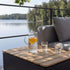 Utomhusbord i teak med förvaring intill en grå loungesoffa på en terrass vid sjön med kanna och glas för en avkopplande stund utomhus från sackit
