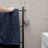 Liten portabel sackit högtalare med träsidor och grå textil hänger på en svart handdukshållare i ett stilrent badrum med kakel