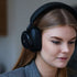 Kvinna med långt hår bär svarta trådlösa over ear hörlurar från sackit för en fokuserad ljudupplevelse hemma#+#+#+#+