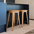Två barstolar i massiv ek med runda sitsar och svarta fotstöd vid en modern köksö designade av sackit för nordisk inredning