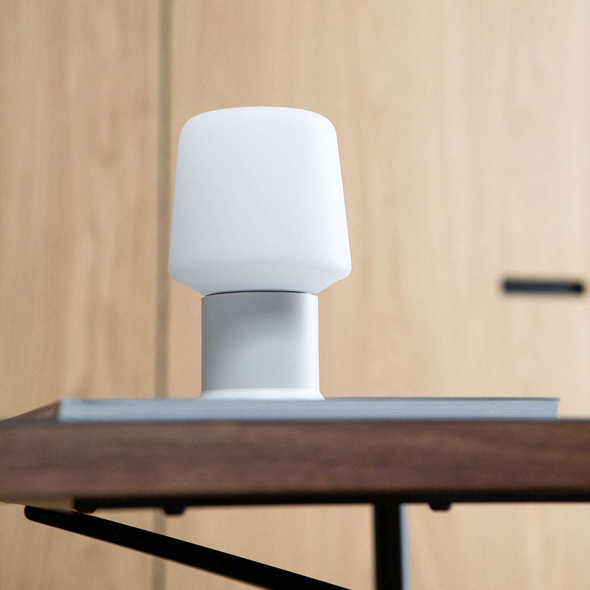 Vit trådlös bordslampa från sackit med rundad lampskärm och låg bas på ett träbord i en modern nordisk interiör