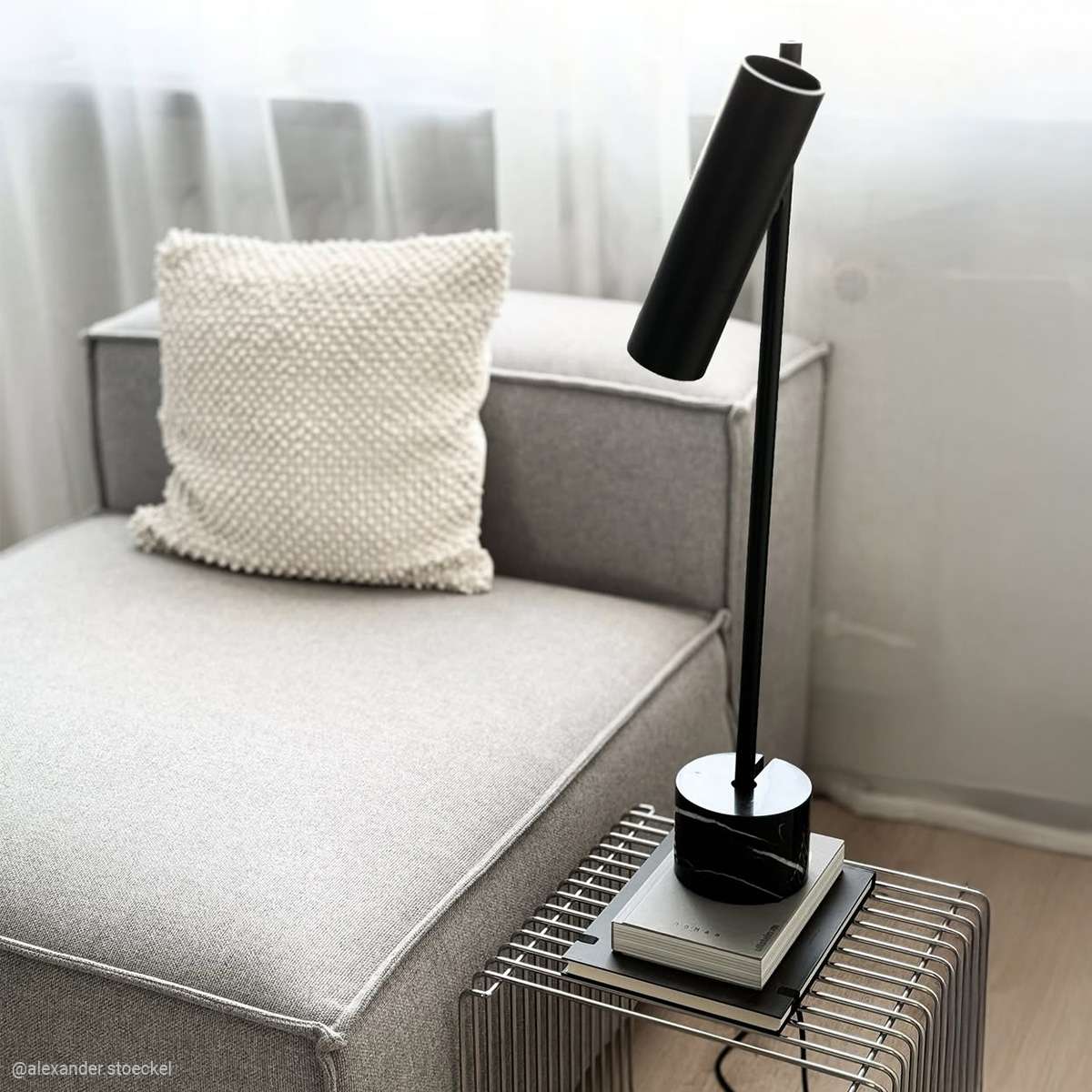 Svart bordslampa med slank aluminiumprofil och marmorfot på ett sidobord i ett ljust vardagsrum från sackit