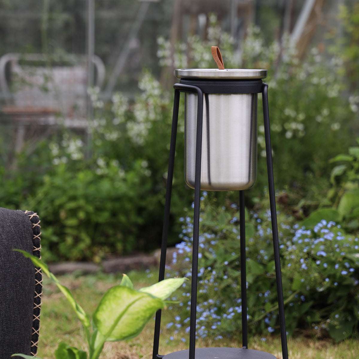 sackit svart tillbehörsstativ för uteplats med cylinderformad vinkylare i rostfritt stål omgivet av grönska och blå blommor