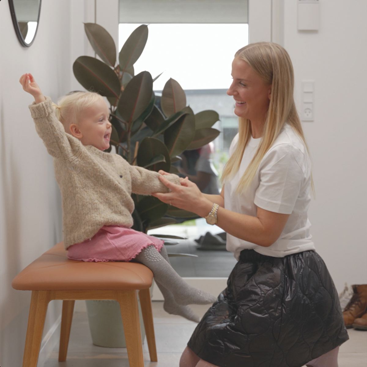 sackit bänk i ek med brunt lädersäte där ett barn leker med en kvinna i ett ljust hem