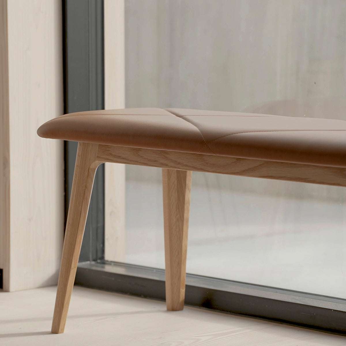 Detaljbild av en nordisk bänk i ek med mjuk brun lädersits och eleganta sömmar från sackit för stilfulla inomhusmiljöer