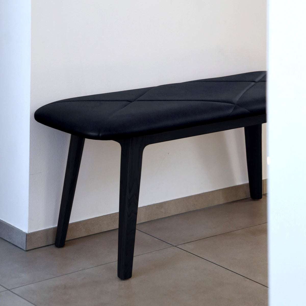 Svart bänk med mjukt lädersäte och släta träben från sackit för stilfulla och bekväma sittplatser i hemmets entré eller vardagsrum