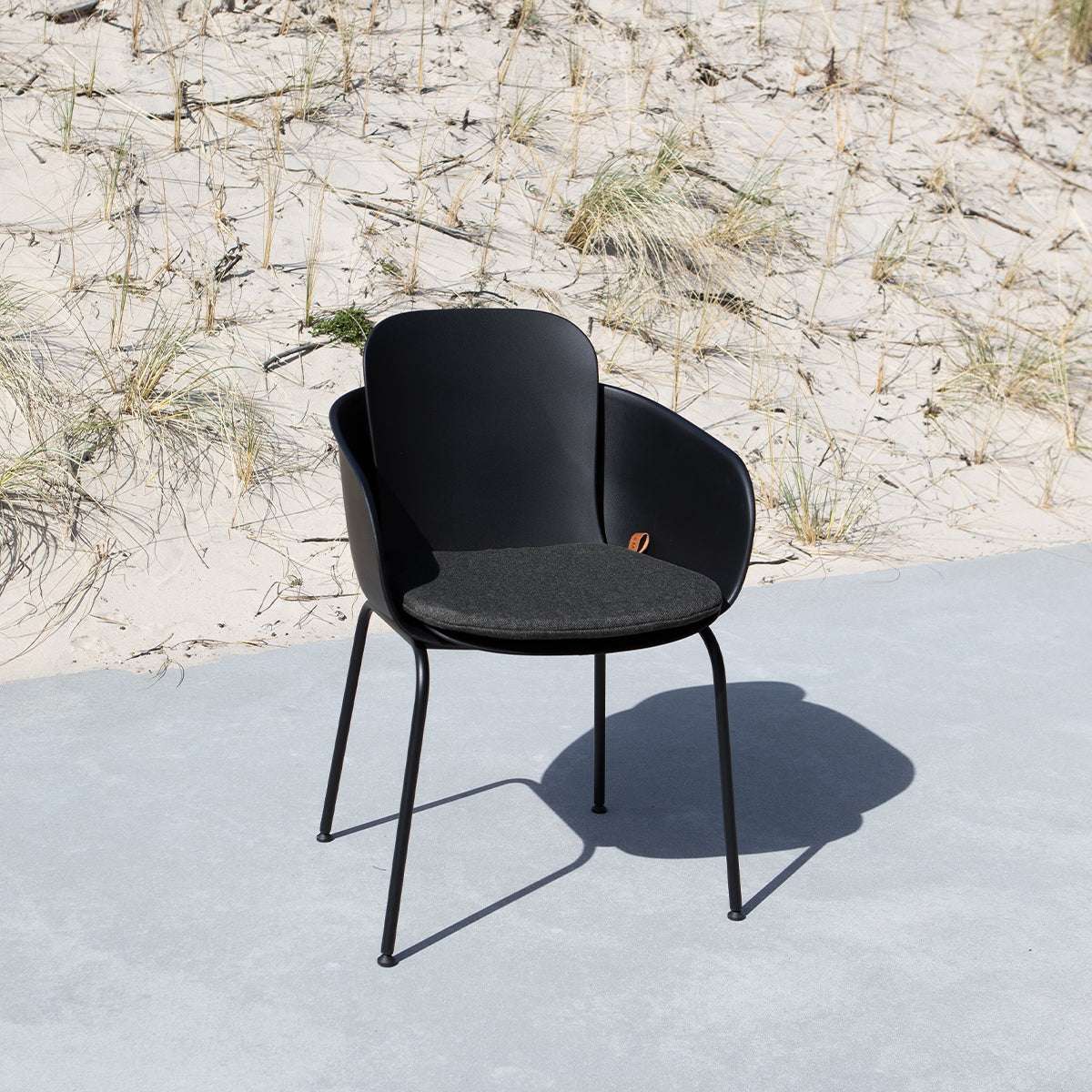 Svart ute stol med anpassad sittdyna från sackit på en solbelyst uteplats vid sanddyner med strandgräs