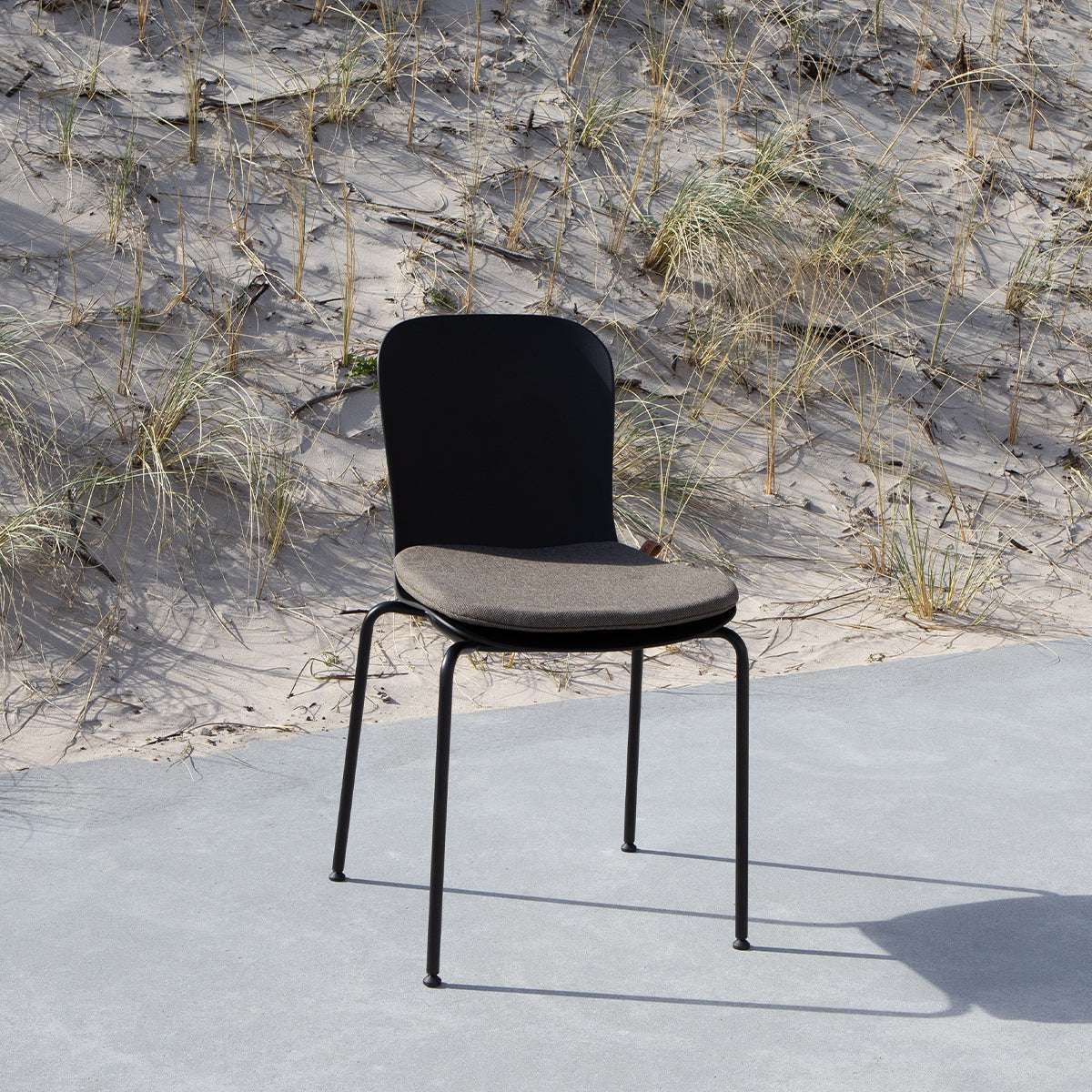 Svart Patio Chair no. One med grå sittdyna från sackit i nordisk utomhusmiljö med sand och strandgräs i bakgrunden