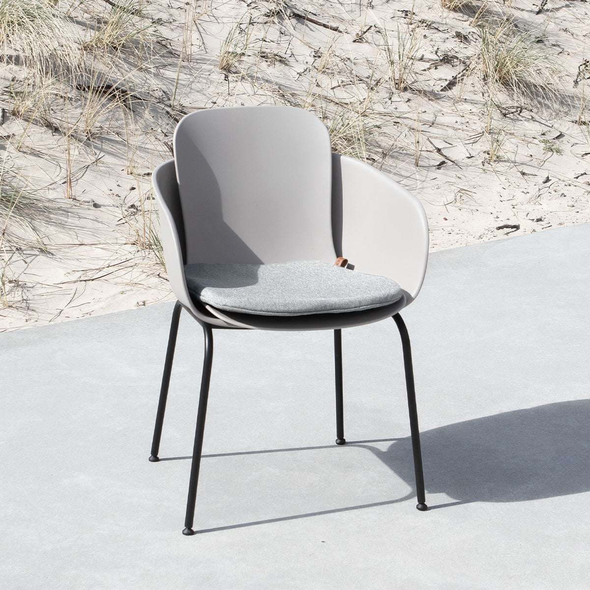 Grå sittdyna på en designad uteplatsstol från sackit i nordisk utomhusmiljö med sanddyner och gräs