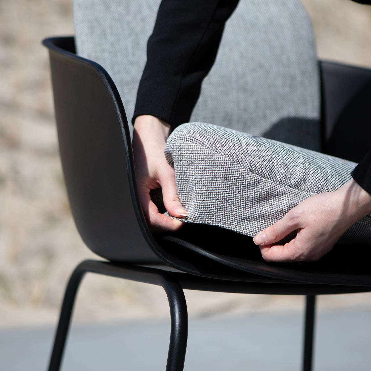 Grå sittdyna i textil placeras på en svart utestol från sackit för bekvämare sittkomfort i nordiskt väder