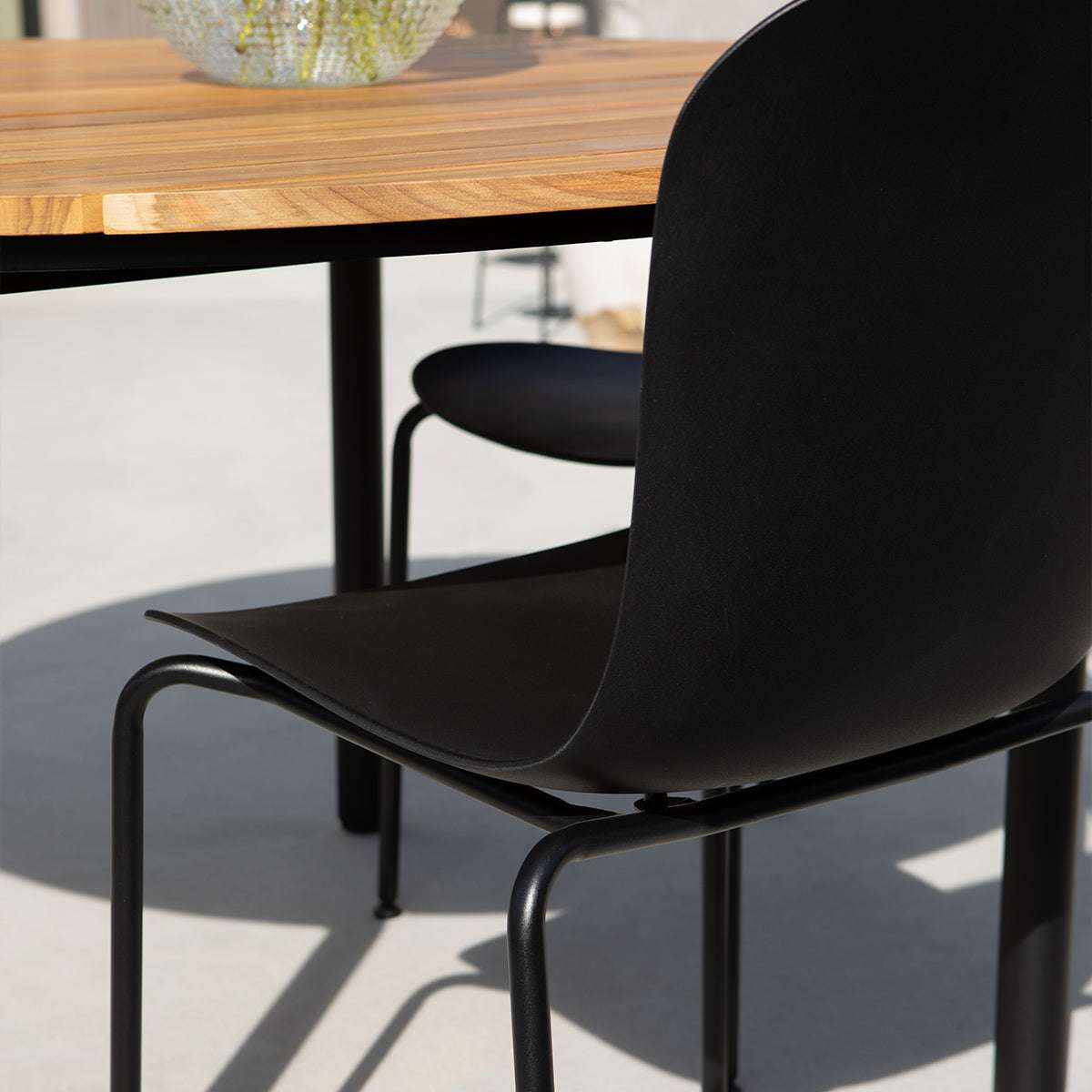 Svart formgjuten uteplatsstol från sackit vid ett träbord på en ljus terrass med nordisk design och bekväm ergonomisk form
