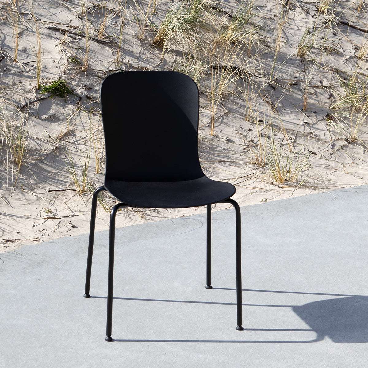 Svart utomhusstol från sackit med ergonomisk formgjuten sits och slanka metallben på en solbelyst uteplats vid sanddynerna