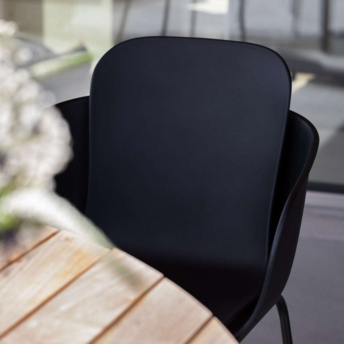 Svart omfamnande utefåtölj från sackit vid ett ljust träbord på en inglasad uteplats nordisk design för bekväma måltider utomhus