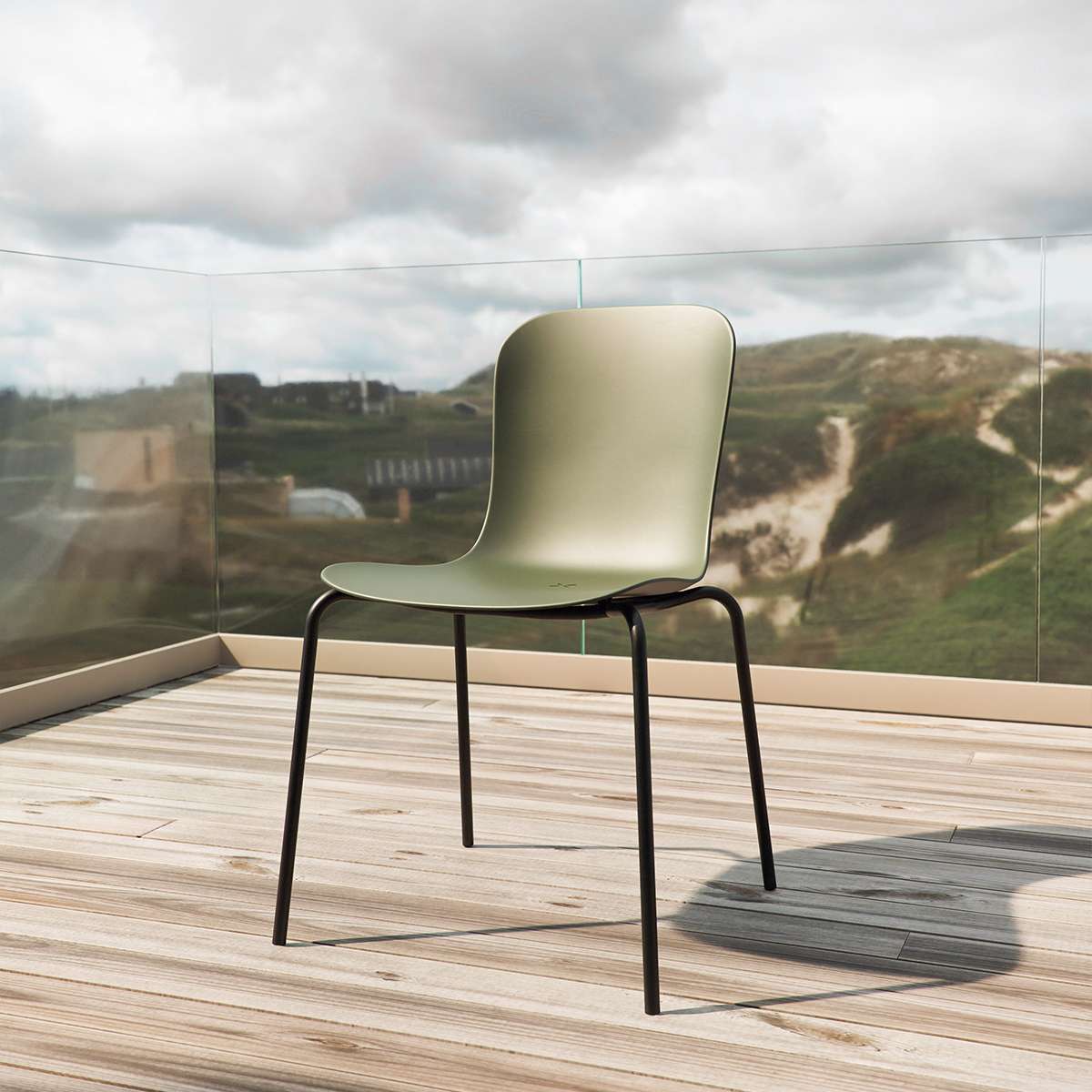 Grön formgjuten uteplatsstol med svart underrede på träaltan och utsikt över kustlandskap. Ergonomisk design från sackit för bekväma stunder utomhus