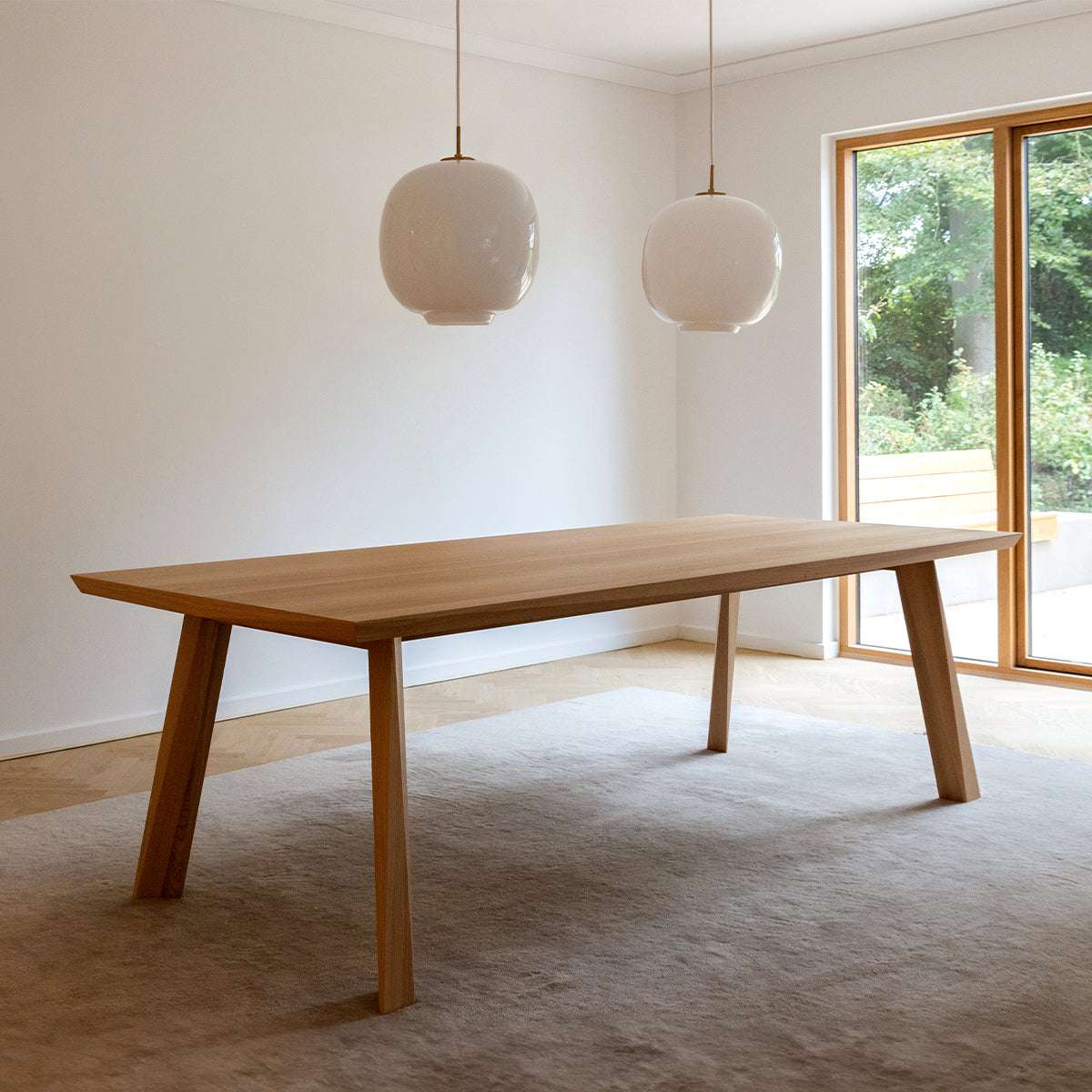 Elegant matbord i europeisk ek med fasetterade detaljer i ett ljust nordiskt matrum med stora fönster och pendellampor från sackit