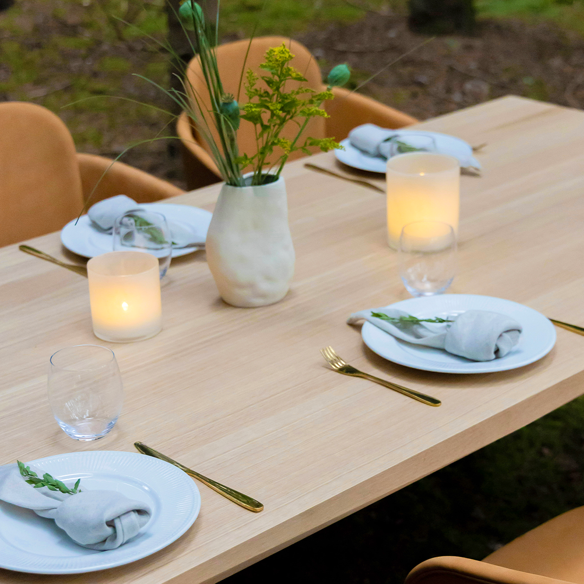Elegant matbord i europeisk ek från sackit med fasetterad bordskant dukat med tallrikar servetter glas ljus och blommor i nordisk utomhusmiljö