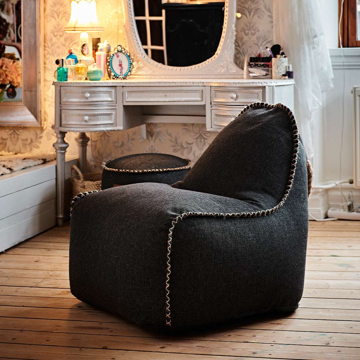 Svart sackit Cobana junior loungefåtölj med matchande puff i ett varmt och klassiskt inrett rum med trägolv dresser och spegel